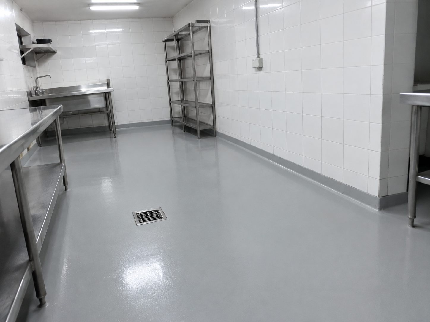 Cocina de hotel con piso epóxico gris continuo, media caña contra el zócalo y rejilla de desagüe embebida en el piso.