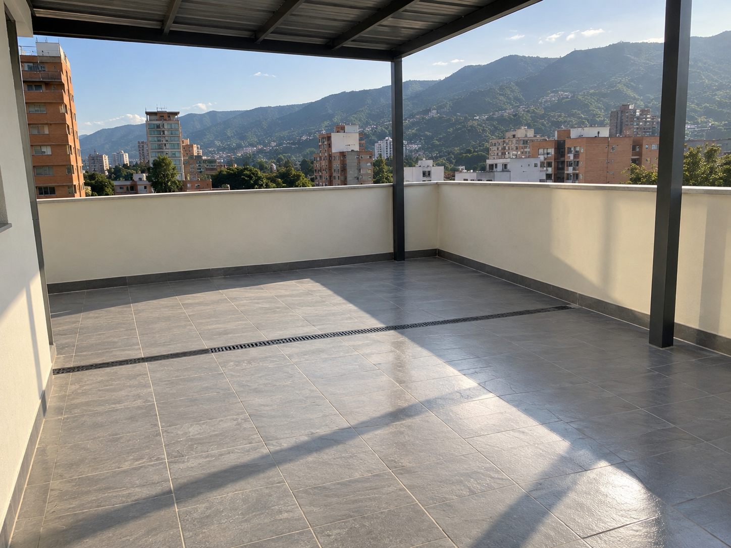 Terraza común cubierta, con piso en porcelanato gris, canal de desagüe lineal y antepecho pintado, sobre los cerros de Medellín.